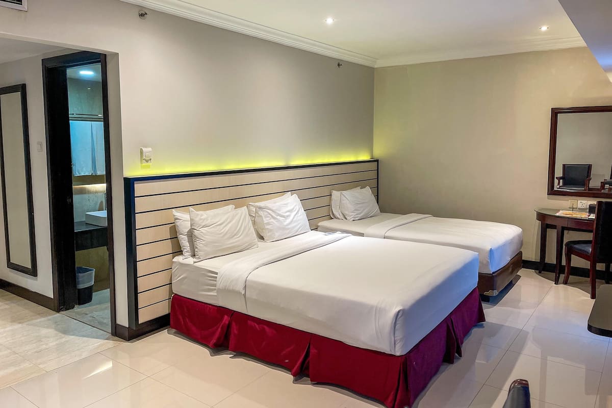 A hotel room with two beds, a desk, a chair, and a mirror.