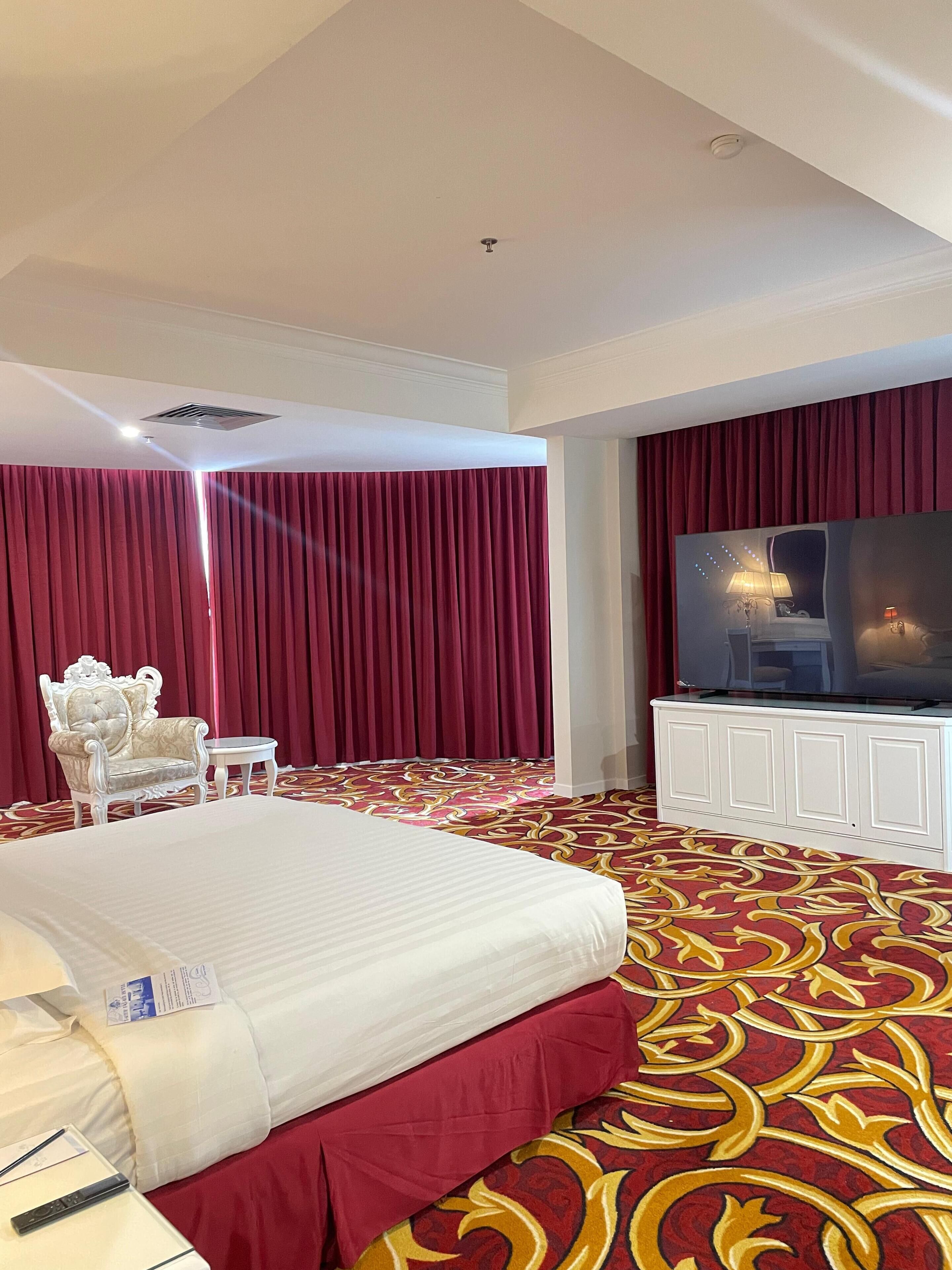 Una habitación de hotel con una cama grande, televisión, alfombra roja y un armario blanco.
