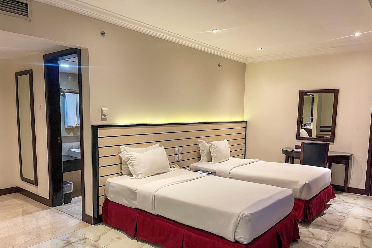 A hotel room with two beds, a desk, a chair, and a mirror.