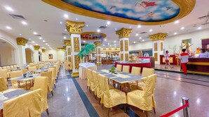A spacious hotel dining area with multiple tables and chairs, a central buffet, and a ceiling mural depicting cherubs. - Pacific Palace Hotel (Batam)