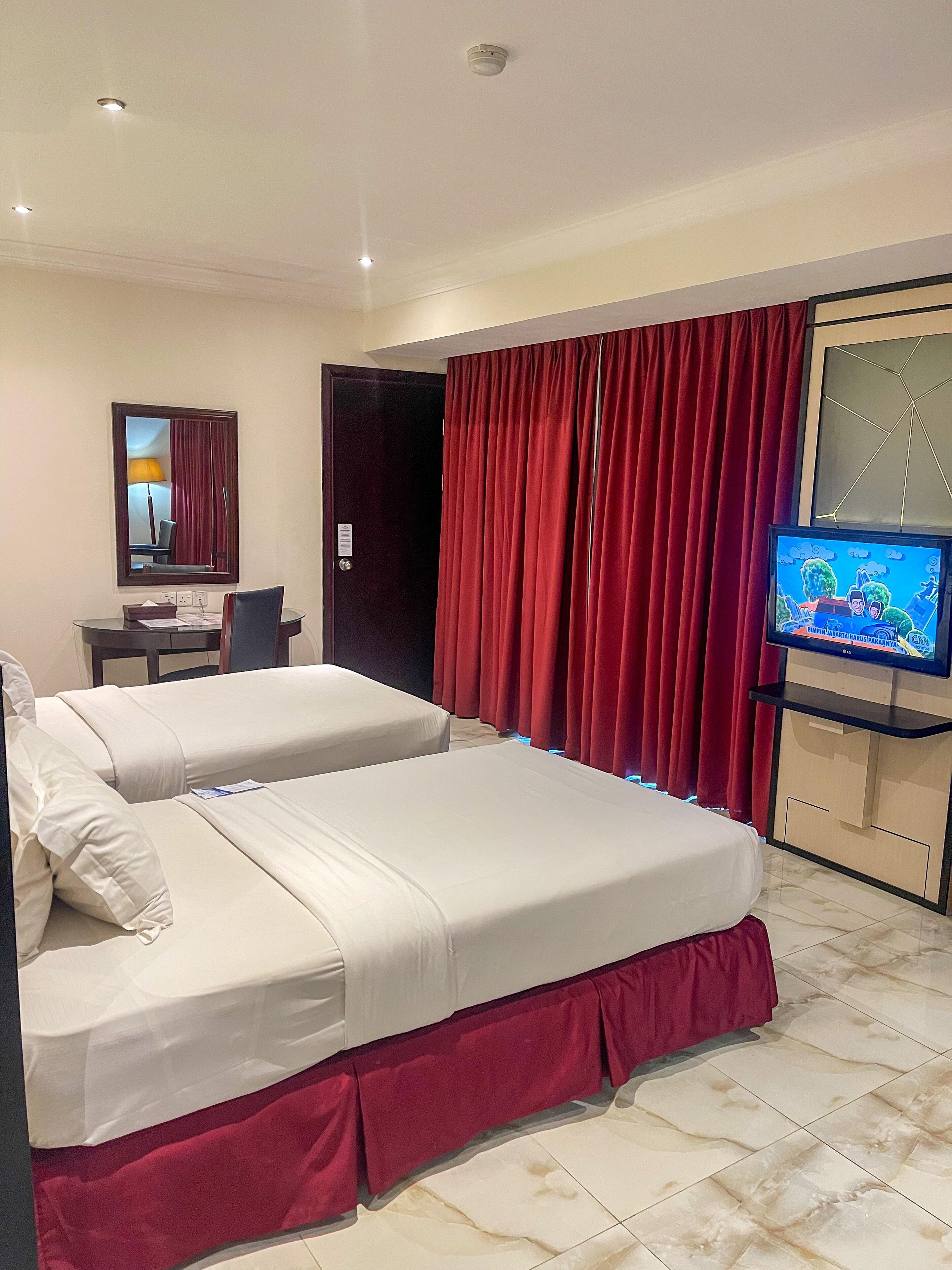 Una habitación de hotel con dos camas, un escritorio, un televisor y un espejo.