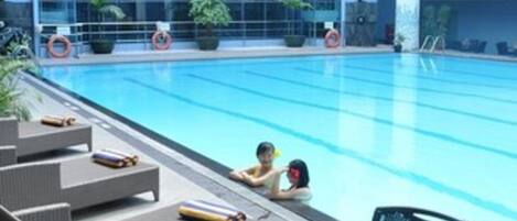 An indoor swimming pool with lounge chairs and a table with fruit and a drink.