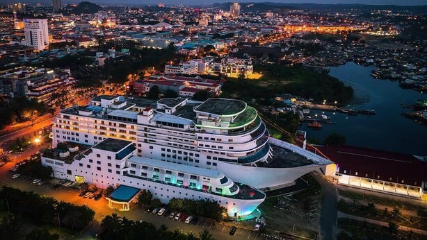 A large cruise ship docked at a port with a modern building nearby. - Pacific Palace Hotel (Batam)