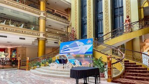A grand lobby with marble floors, a central display of a cruise ship, and a staircase with ornate railings. - Pacific Palace Hotel (Batam)