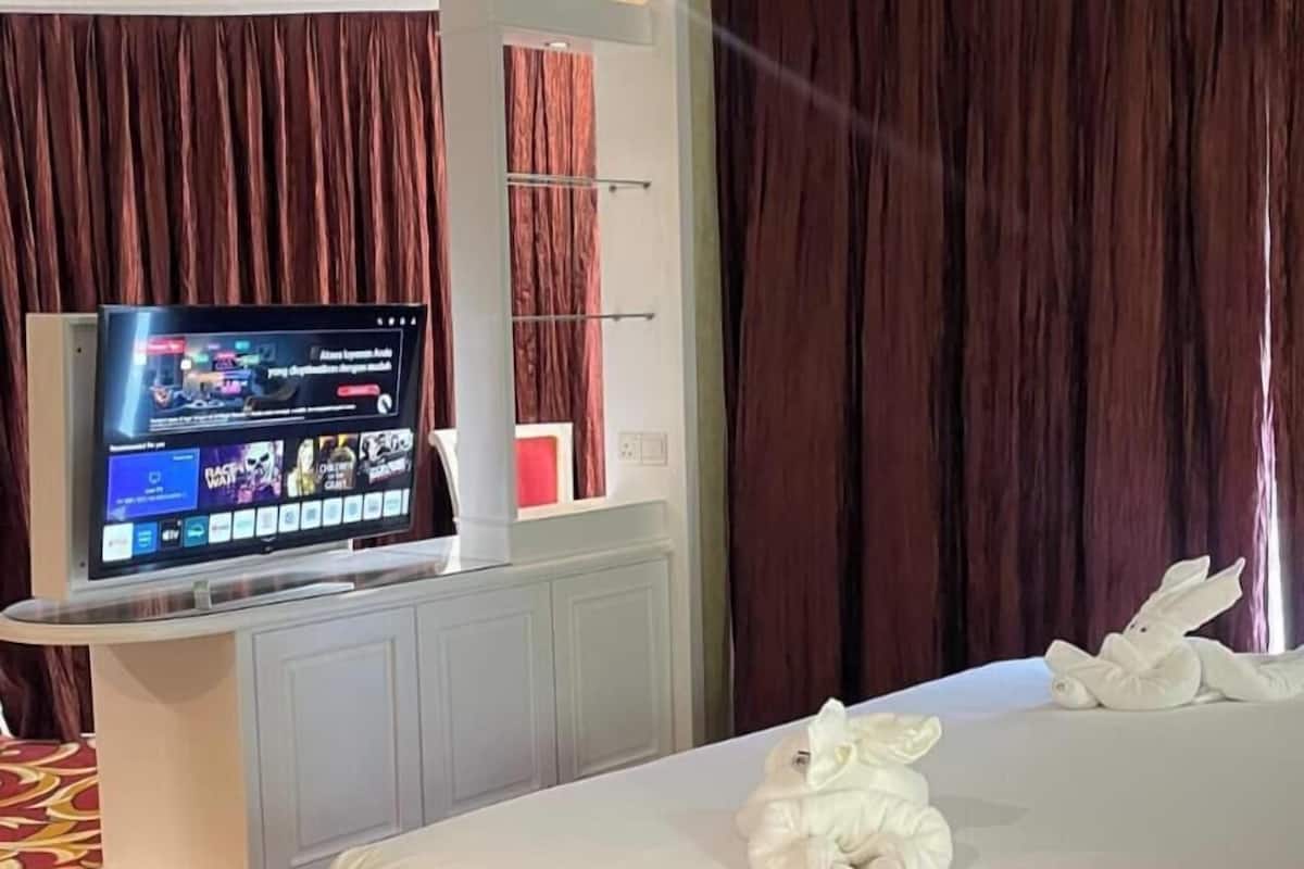 A hotel room with a bed, a TV on a stand, a wardrobe, and a curtain.