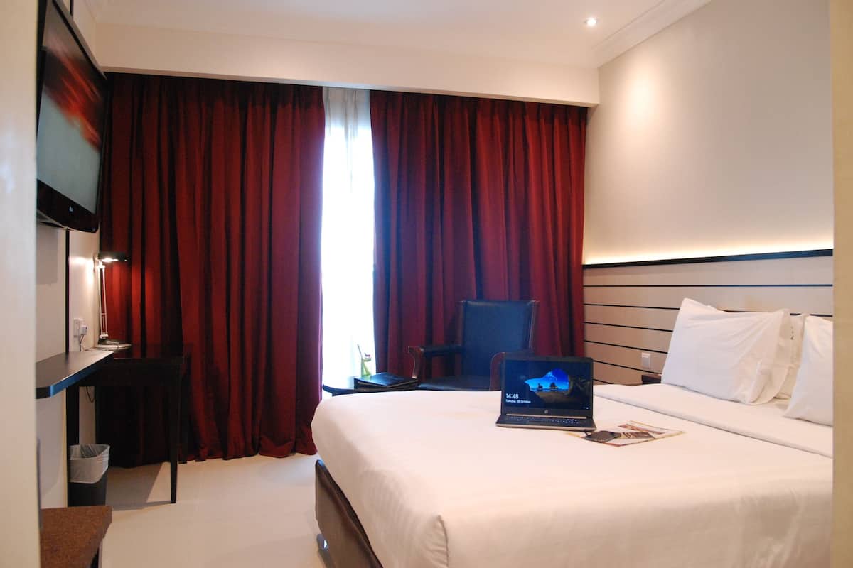 A hotel room with a bed, a desk with a laptop, a chair, and a TV on a stand.