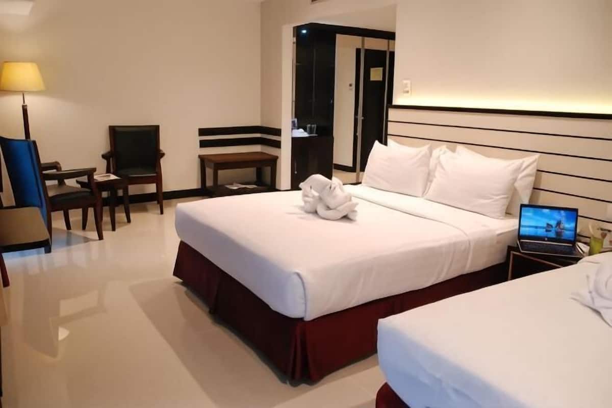 A hotel room with a bed, a desk, a chair, and a laptop.