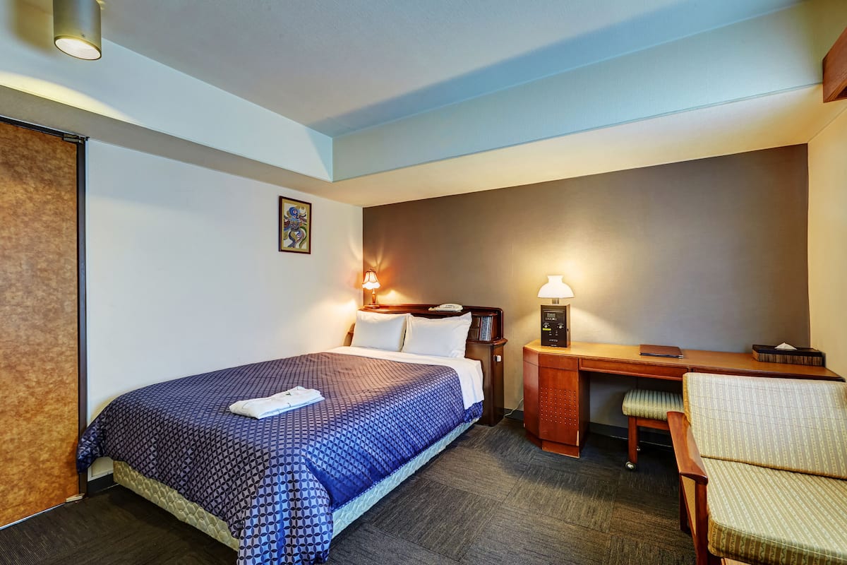 A hotel room with a bed, desk, chair, and bedside lamps.