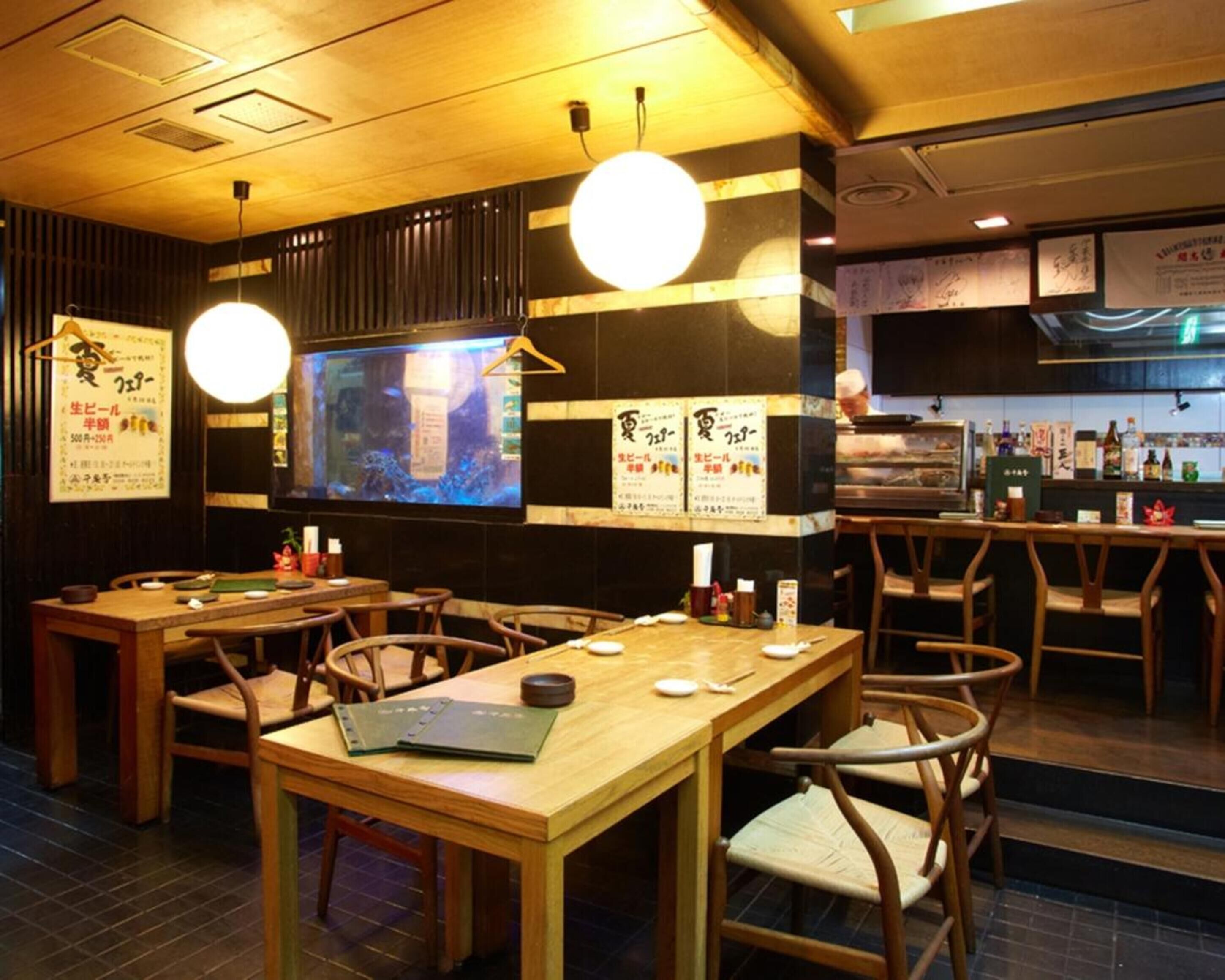 Interior de restaurante con mesas y sillas de madera, una pantalla de televisión grande y varios carteles de menú en las paredes.