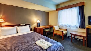 A hotel room with a large bed, a desk, a chair, a small table, and a television. - Hotel Taira (Naha)