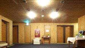 A conference room with a carpeted floor, a white armchair, a small table with a vase and plants, and a framed picture on a table. - Hotel Taira (Naha)