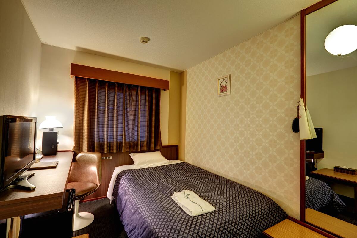 A hotel room with a bed, a desk with a lamp, a chair, and a mirror.