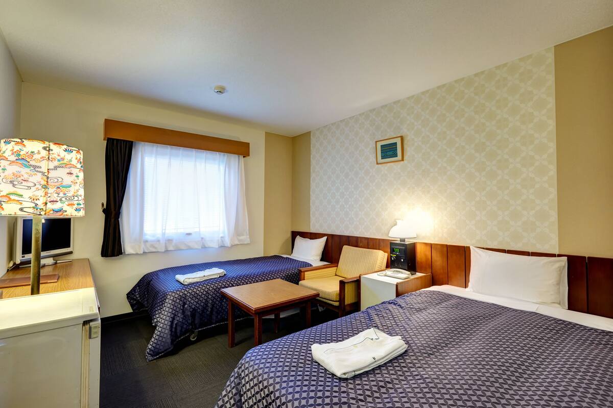 A hotel room with two beds, a desk, a chair, a TV, and a lamp.
