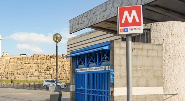 Entrada de una estación de metro con una puerta azul, un muro de piedra grande y un cielo despejado.