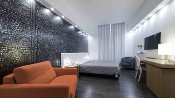 A modern hotel room with a bed, a desk, a chair, and a sofa.
