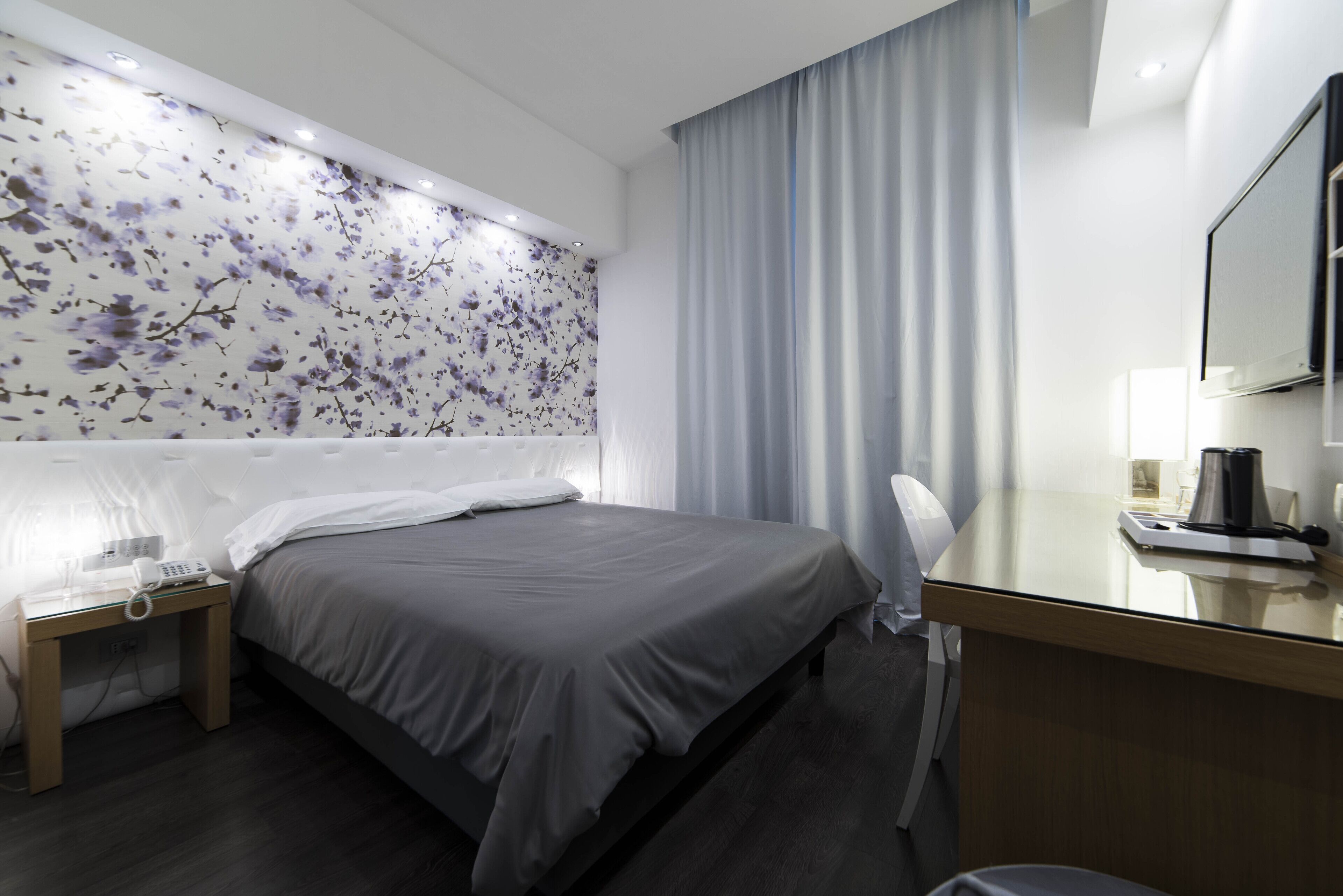 Habitación de hotel con cama, escritorio, silla, teléfono, lámpara y espejo.