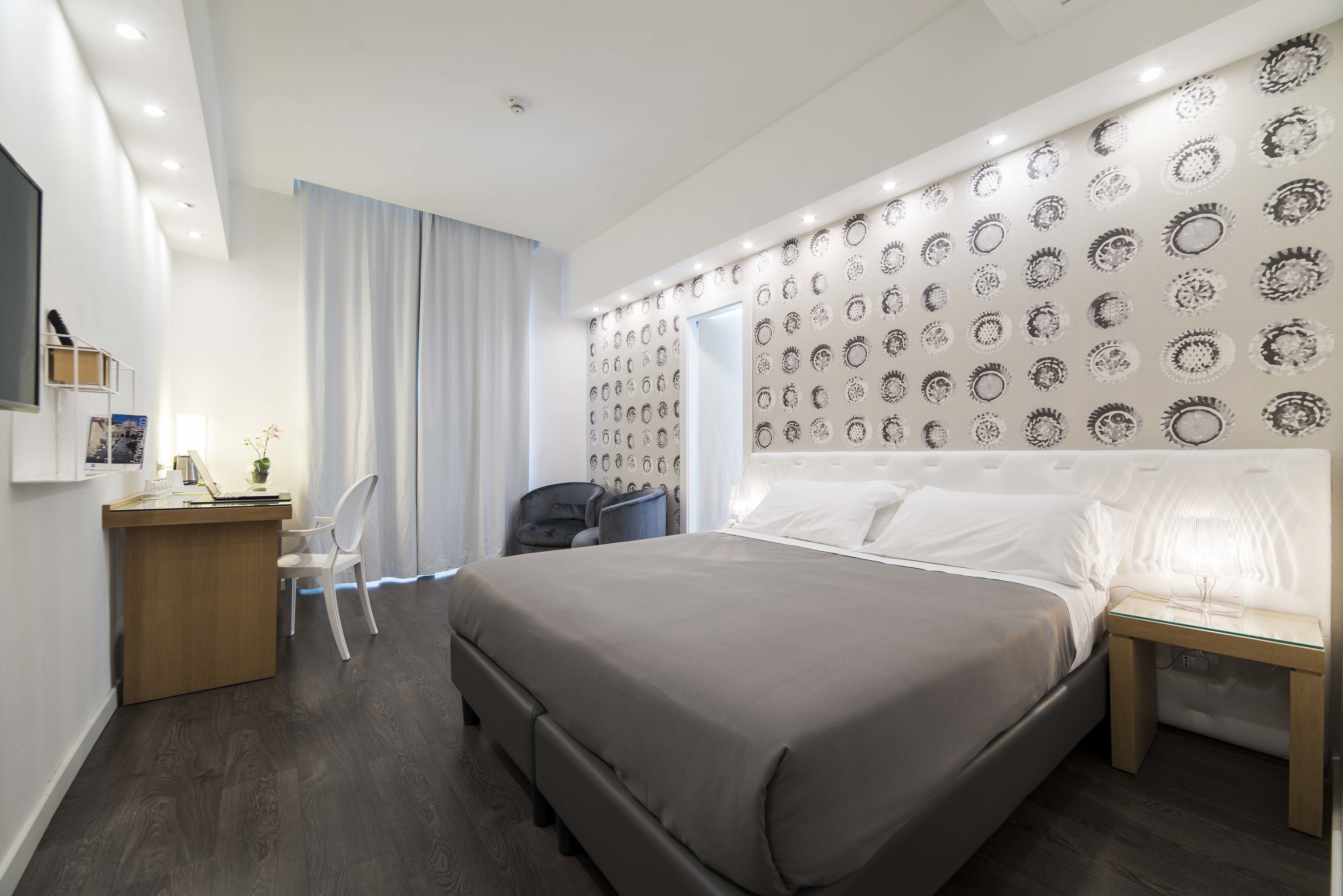 Una habitación de hotel moderna con una cama grande, un escritorio con una silla, una mesita pequeña y una pared con diseños circulares.