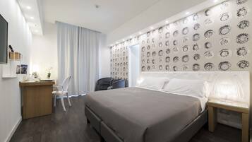 A modern hotel room with a large bed, a desk with a chair, a small table, and a wall with circular patterns.