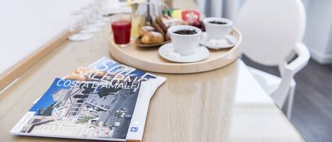 A breakfast table with a magazine, pastries, coffee, and a red drink.