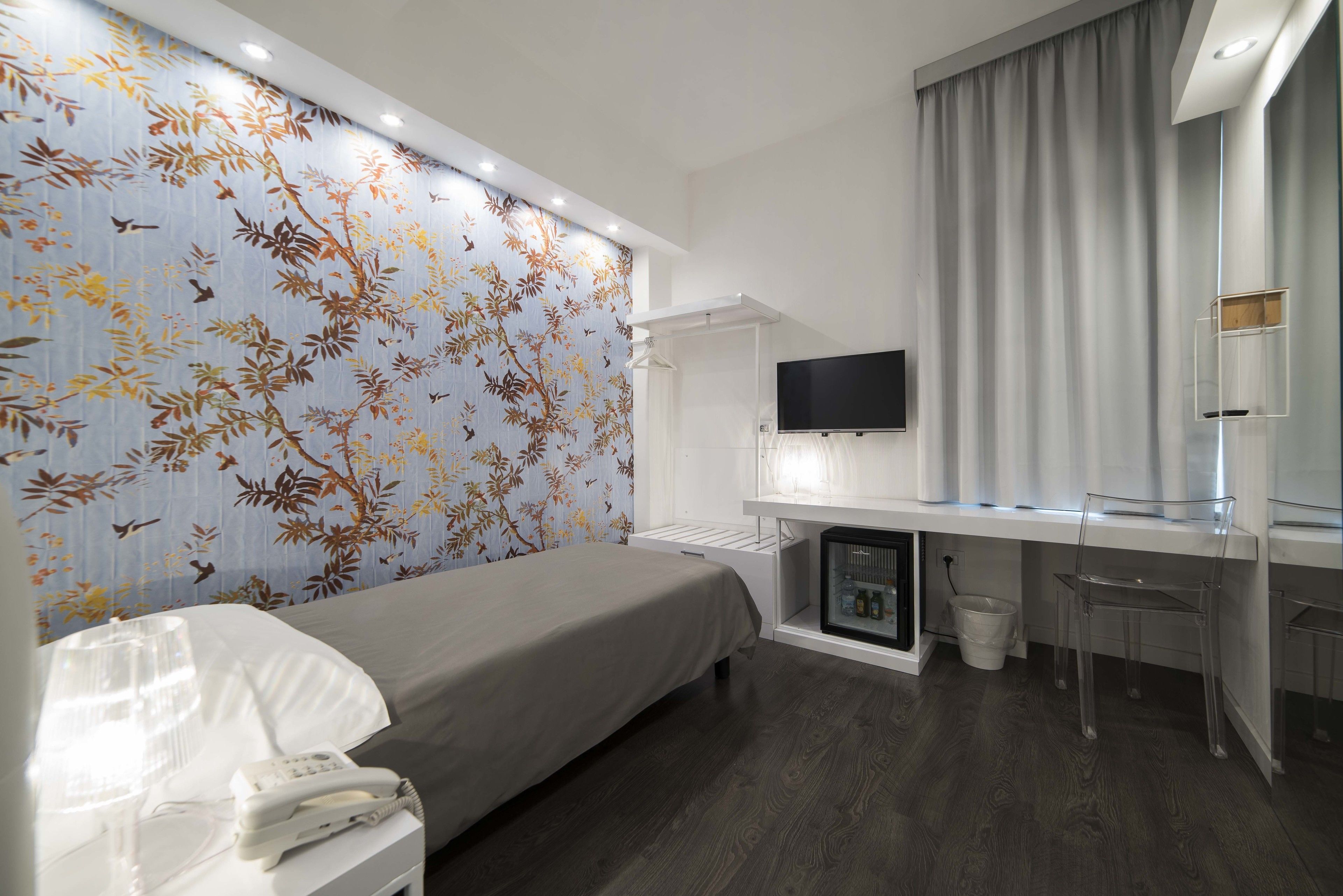 Une chambre d’hôtel moderne équipée d’un lit, d’un bureau avec un ordinateur, d’une télévision et d’un mini-bar.