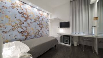Une chambre d’hôtel moderne équipée d’un lit, d’un bureau avec un ordinateur, d’une télévision et d’un mini-bar.