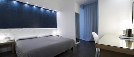 A modern hotel room with a large bed, a desk with a chair, and a large window with curtains.