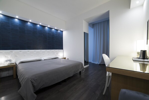 A modern hotel room with a large bed, a desk with a chair, and a large window with curtains. - Hotel Montestella (Salerno)
