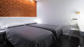 Une chambre d’hôtel avec deux lits, un bureau, une chaise et un mur orné d’un motif géométrique.