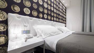 Una habitación de hotel moderna con papel tapiz estampado, un cabecero blanco, una mesita de noche con un teléfono y una cama gris.