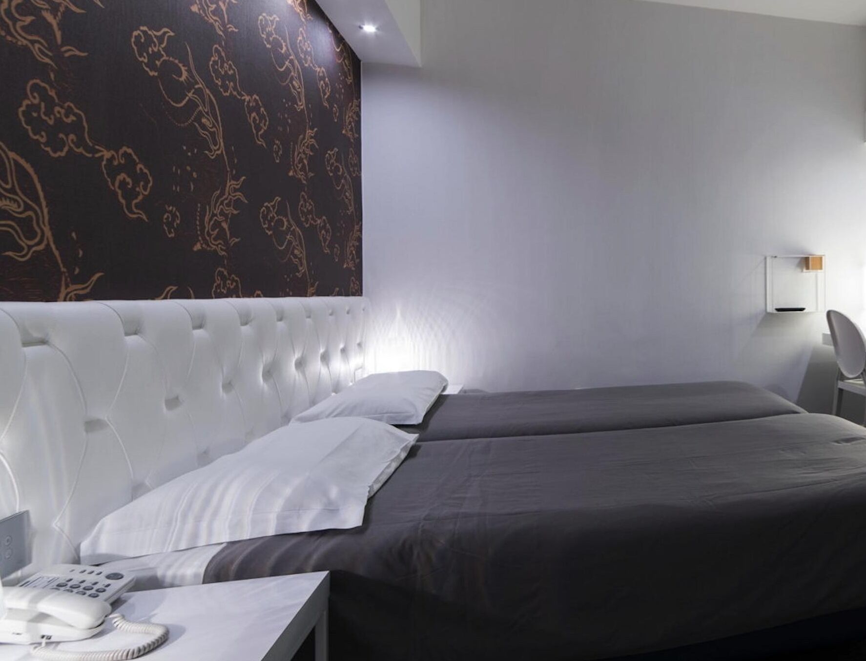 A modern hotel room with a large bed, a bedside telephone, and a wall-mounted light fixture.