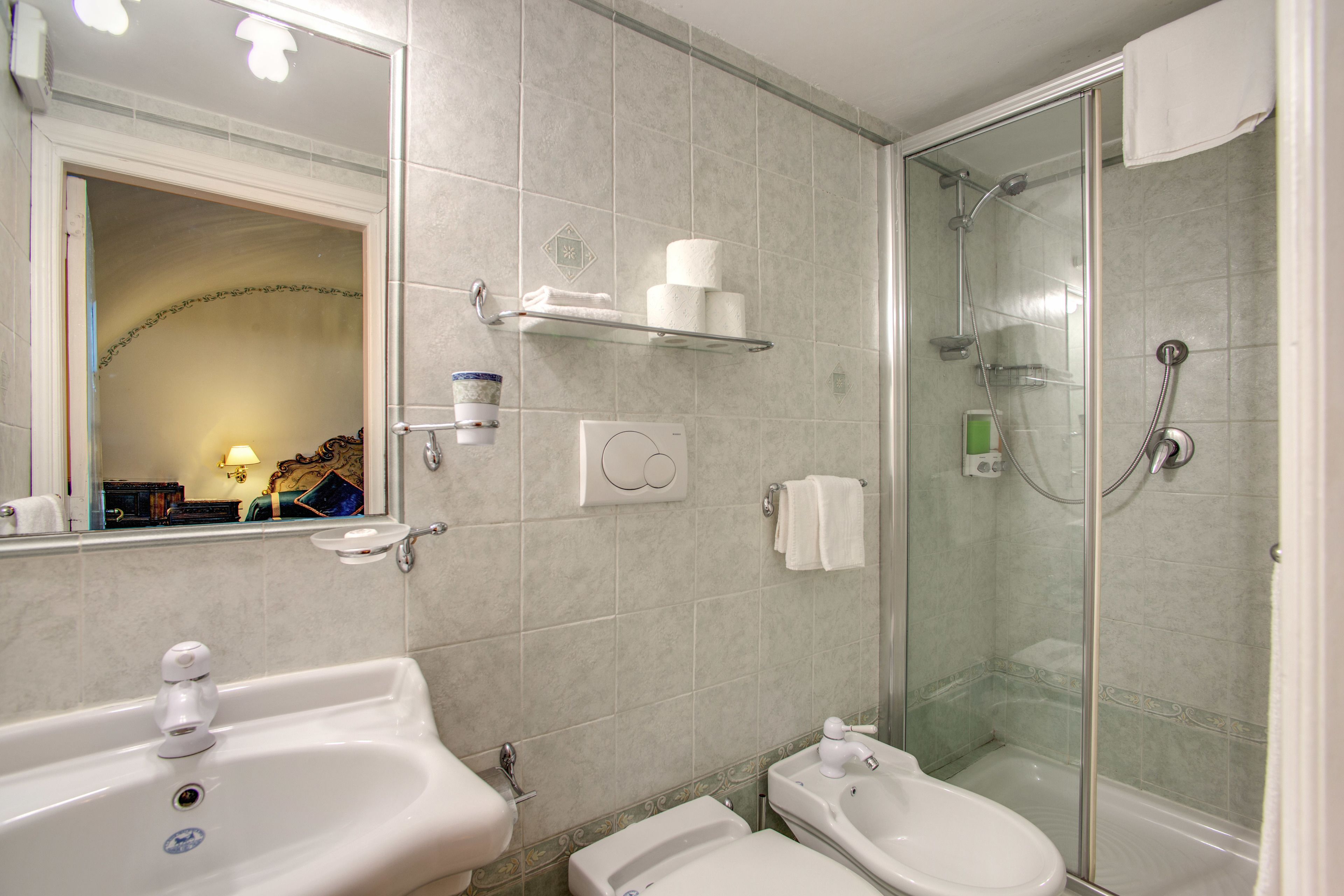 Baño con lavamanos, inodoro y ducha con mampara de vidrio.