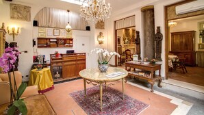 A spacious living room with a high ceiling, a chandelier, a round table with a vase of flowers, and a large window providing natural light. - Navona Gallery Suites (Rome)