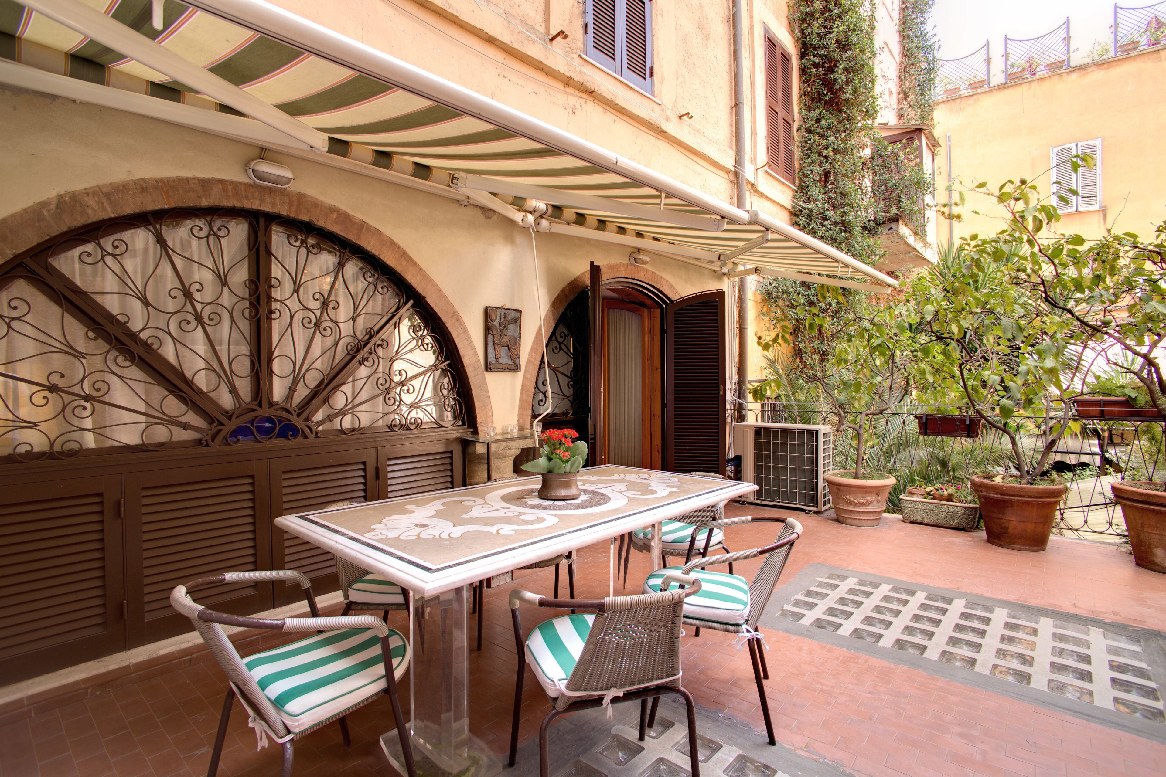An outdoor patio with a table and chairs, a decorative metal gate, potted plants, and a tiled floor.