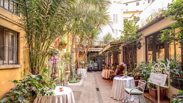 A courtyard with tables and chairs, surrounded by plants and a 'Welcome' sign. - Navona Gallery Suites (Rome)