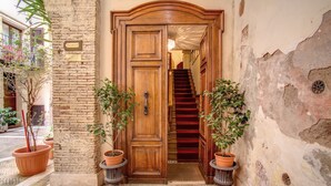 A wooden door with a red carpet leading to a staircase. There are potted plants on either side of the door. - Navona Gallery Suites (Rome)