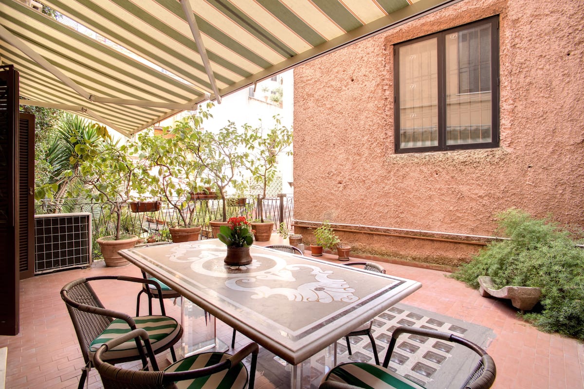 An outdoor patio with a table and chairs, surrounded by potted plants and a brick wall.