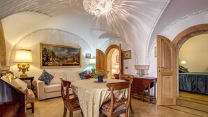 A dining area with a round table, chairs, and a chandelier. There is a painting on the wall and a door leading to another room. - Navona Gallery Suites (Rome)