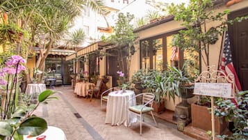 Eine Terrasse im Freien mit Tischen und Stühlen, umgeben von Blumentöpfen und einem Schild mit der Aufschrift 'Welcome'.