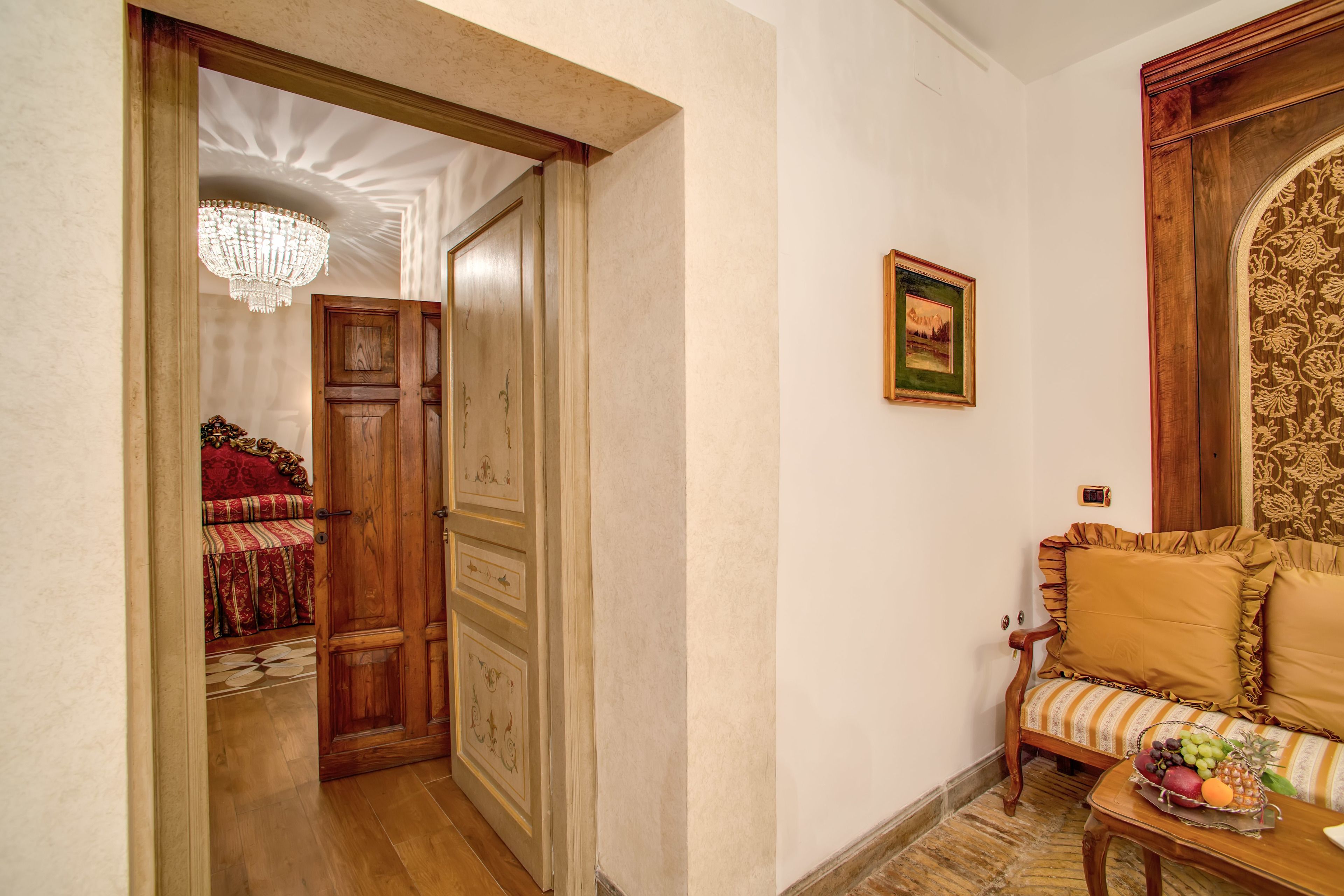 A hallway with a wooden door, a chandelier, a sofa with patterned cushions, and a fruit basket on a small table.