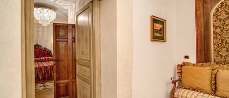 A hallway with a wooden door, a chandelier, a sofa with patterned cushions, and a fruit basket on a small table.