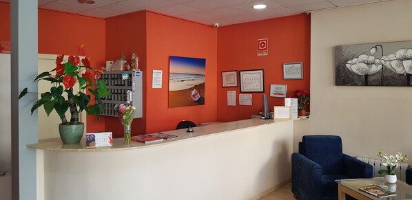 Een receptiegedeelte met een rode muur, een receptiebalie, een blauwe stoel en een potplant.