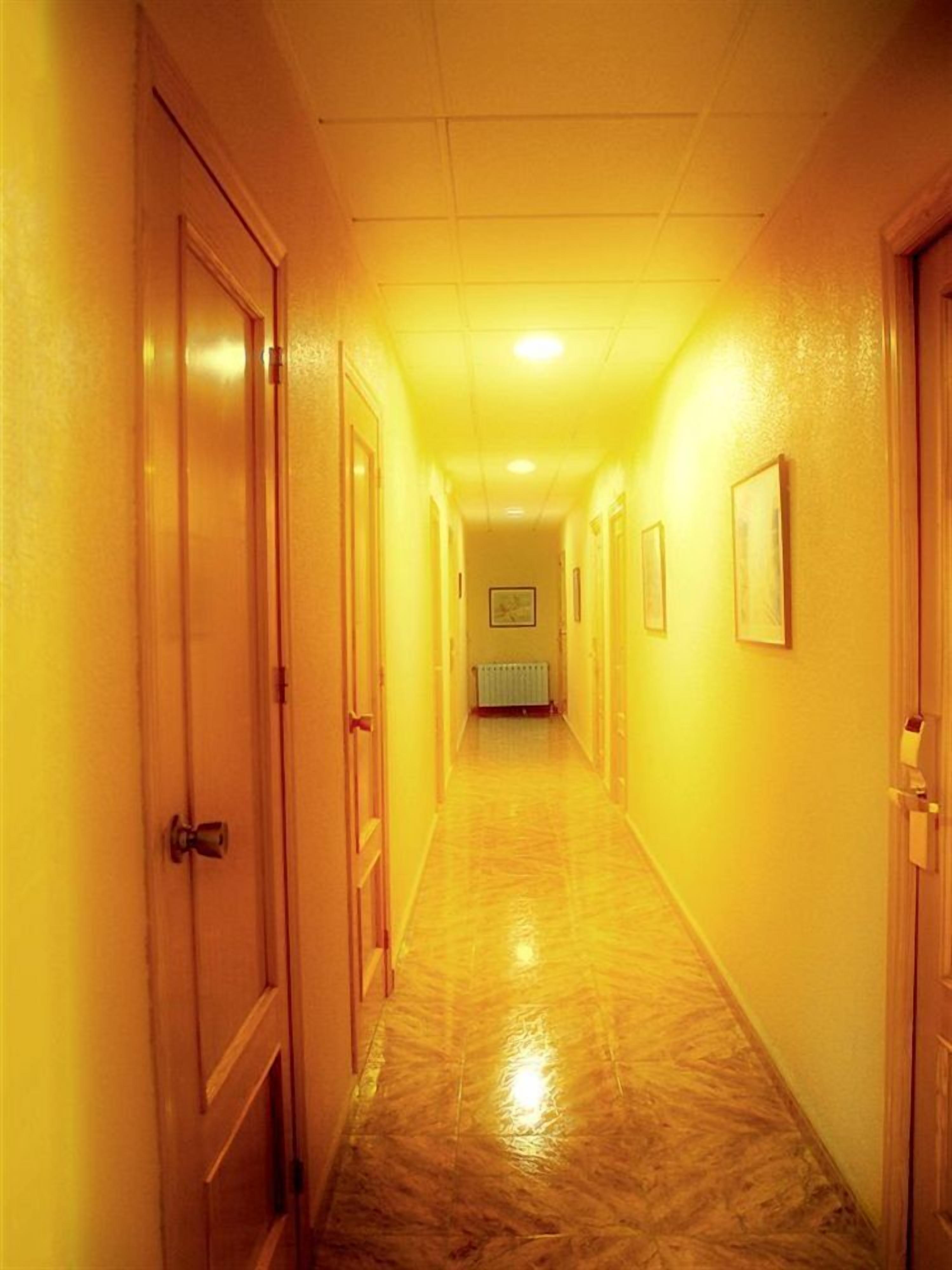 A hallway with wooden doors on both sides, a tiled floor, and framed pictures on the walls.