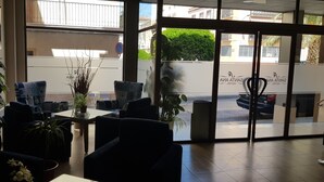 Un hall d’hôtel avec des sièges, des plantes en pot et une vue sur la rue.
