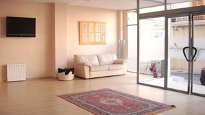 Une pièce spacieuse avec un canapé beige, un tapis à motifs, un téléviseur à écran plat et une fenêtre donnant sur l’extérieur.