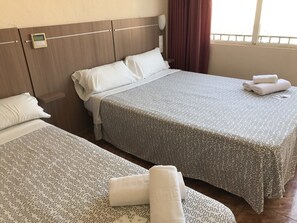 Hotelkamer met twee bedden, elk voorzien van beddengoed en kussens, een nachtkastje en een raam met gordijnen.