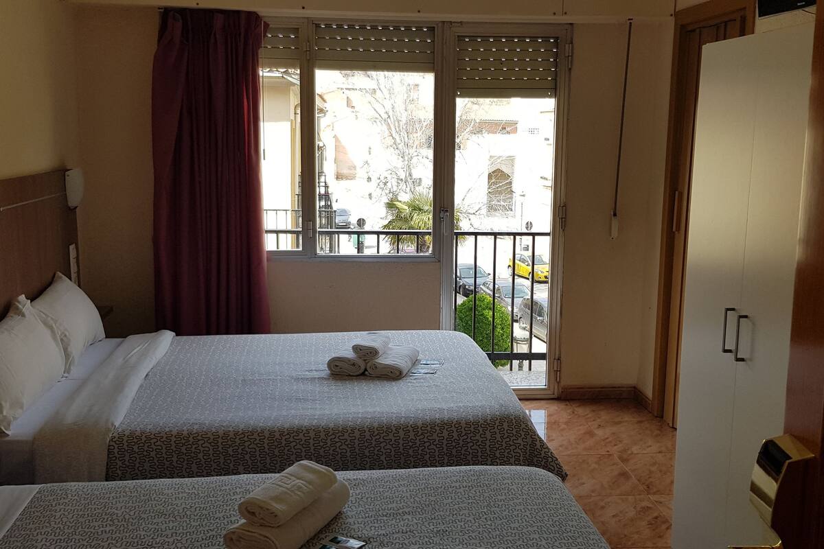 A hotel room with two beds, a balcony with a view of the street, and a wardrobe.
