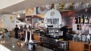 L’intérieur d’un café, avec une machine à café, des étagères remplies de bouteilles et des verres suspendus.
