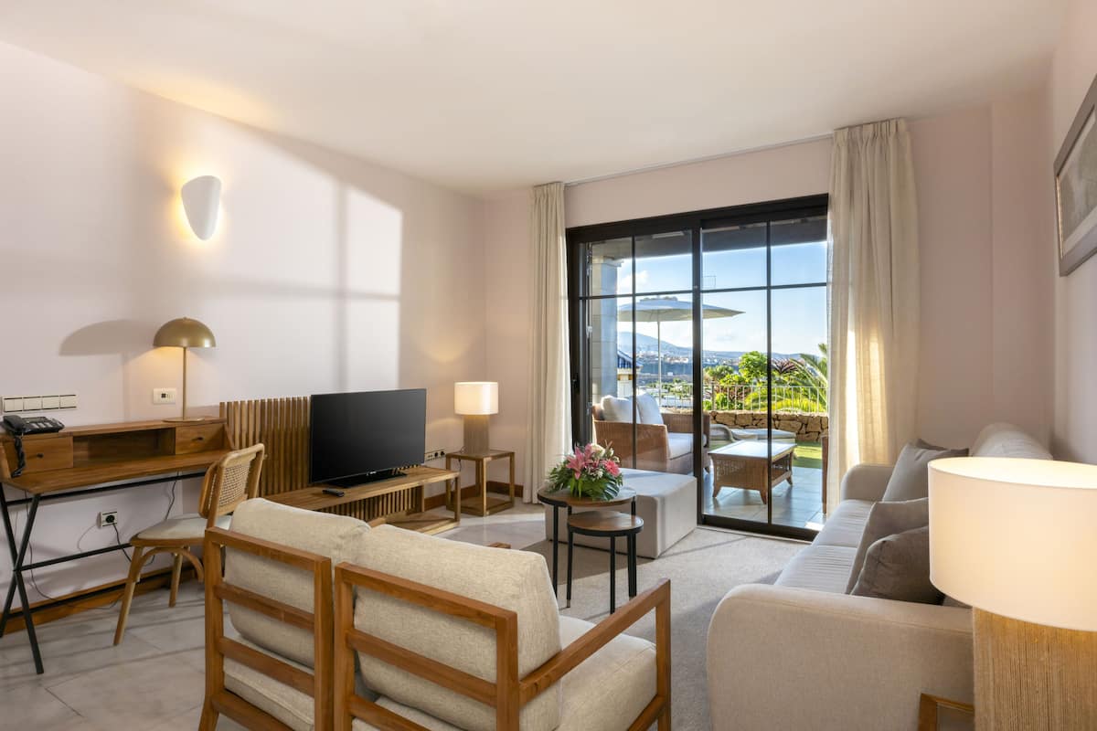 Una habitación de hotel moderna con un escritorio de madera, un televisor de pantalla plana, un sofá y un balcón con vistas a la ciudad.