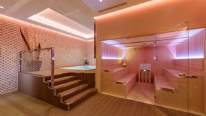 Un spa moderno con suelos de madera, una sauna con paredes de vidrio y una bañera de hidromasaje a la vista.