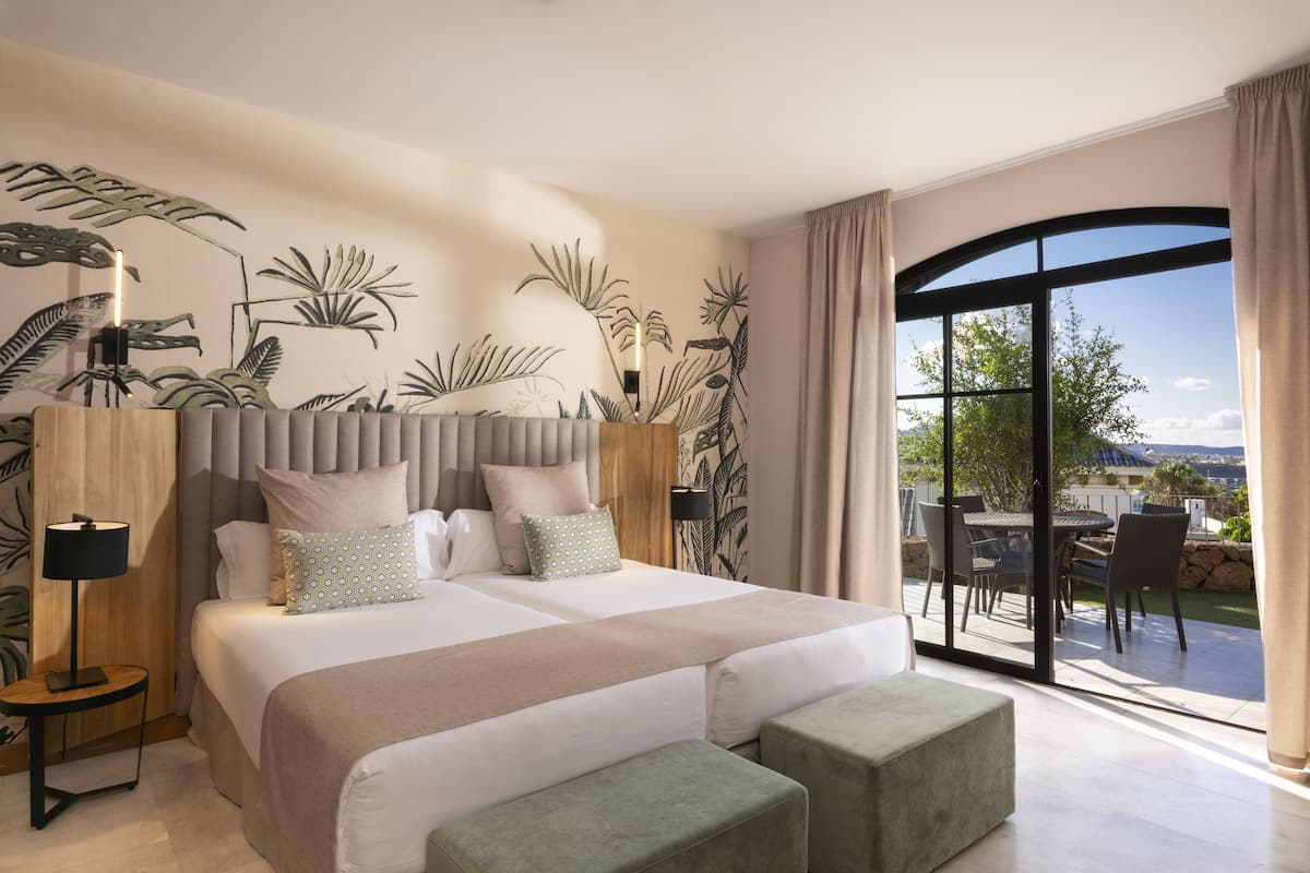 Un dormitorio amplio con una cama grande, un balcón con mobiliario exterior y vistas del paisaje.